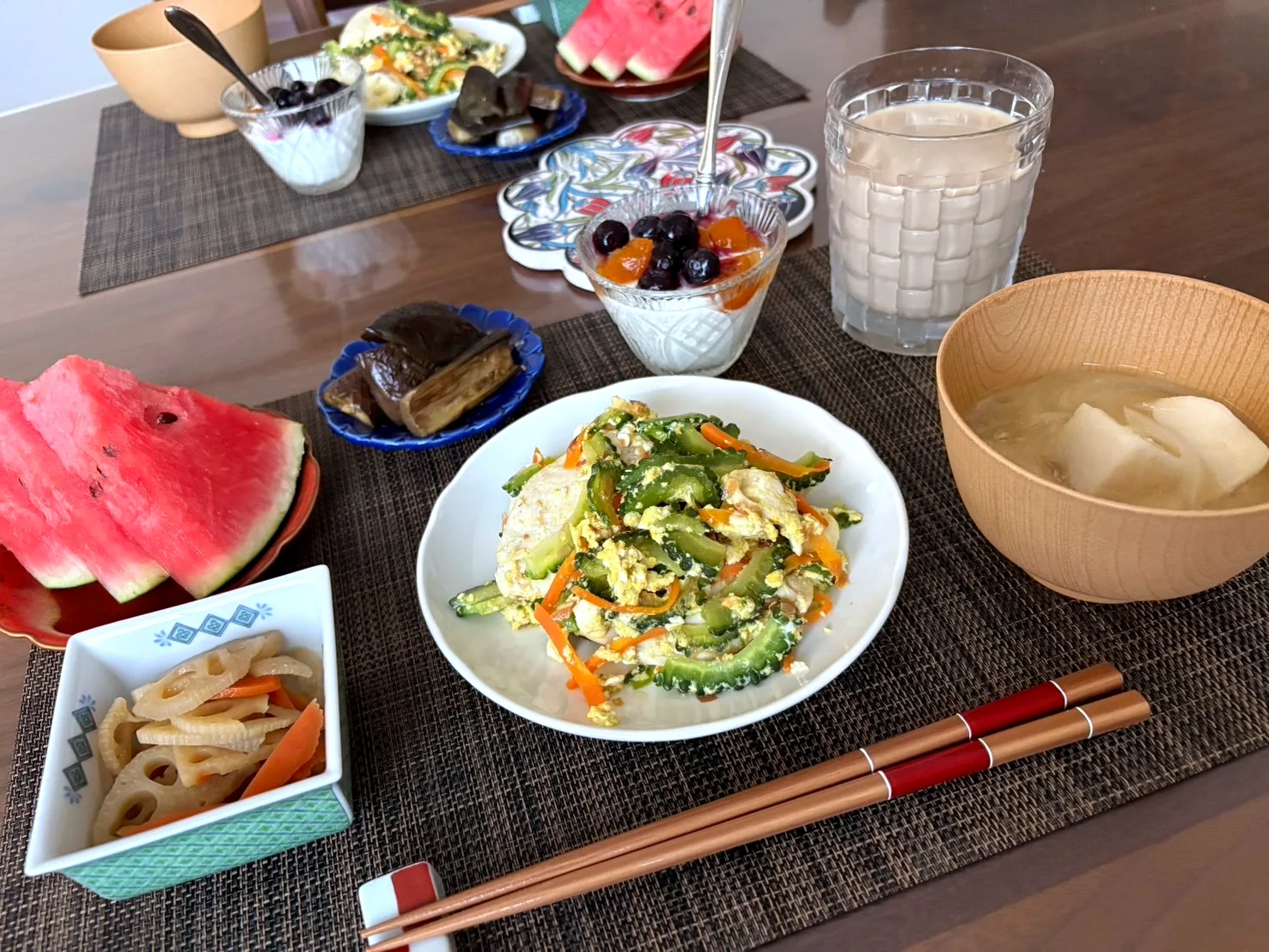 Japanese breakfast tray with stir-fried bitter melon, simmered lotus root and carrot, miso soup in a wooden bowl, watermelon and yogurt