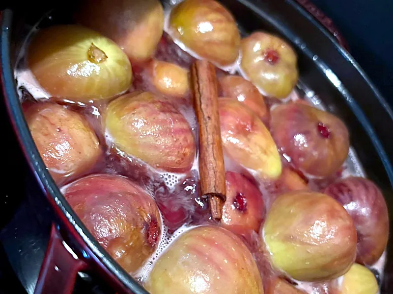 Whole figs simmering in a dark red enamel pot with a cinnamon stick, for fig compote