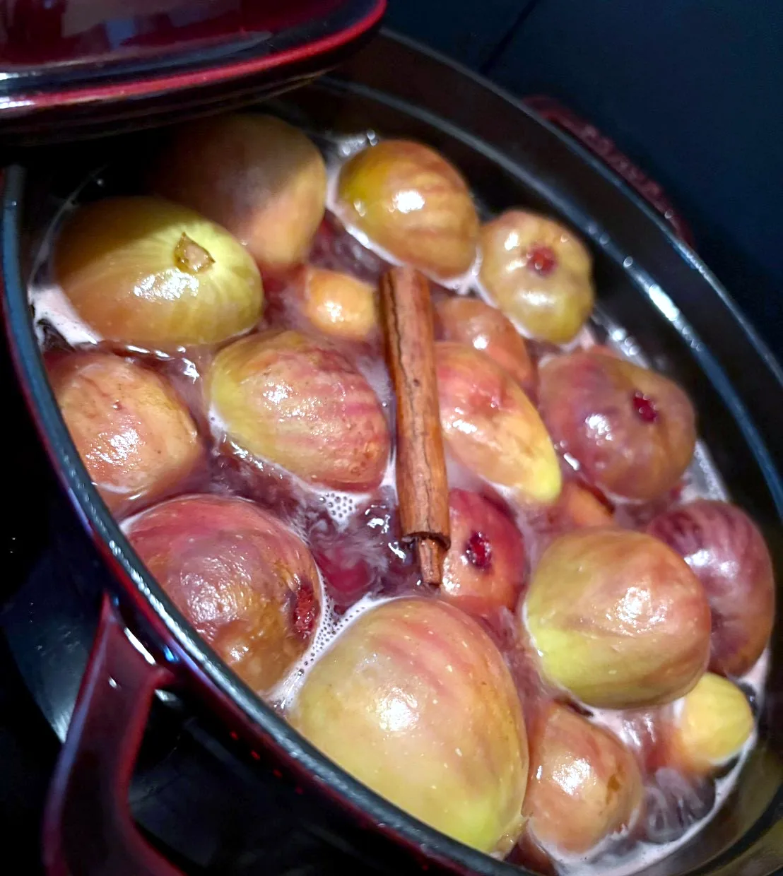 Whole figs simmering in a dark red enamel pot with a cinnamon stick, for fig compote