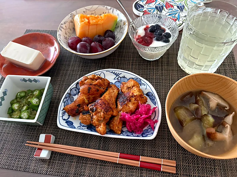 Japanese breakfast tray with grilled chicken and pink pickles, okra, tofu, mushroom miso soup in a wooden bowl, melon, grapes and yogurt