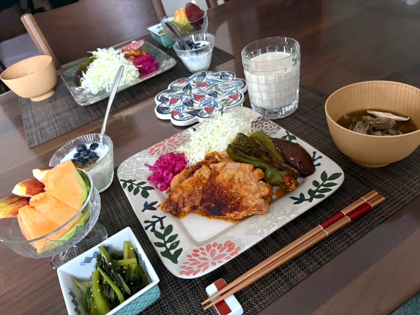 Japanese breakfast tray with grilled meat and shredded cabbage on a patterned plate, soup in a wooden bowl, melon, greens and yogurt