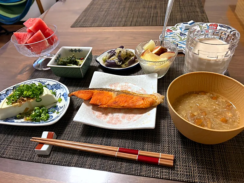 Japanese breakfast with grilled salmon, cold tofu topped with green onion, soup in a wooden bowl, small side dishes and watermelon