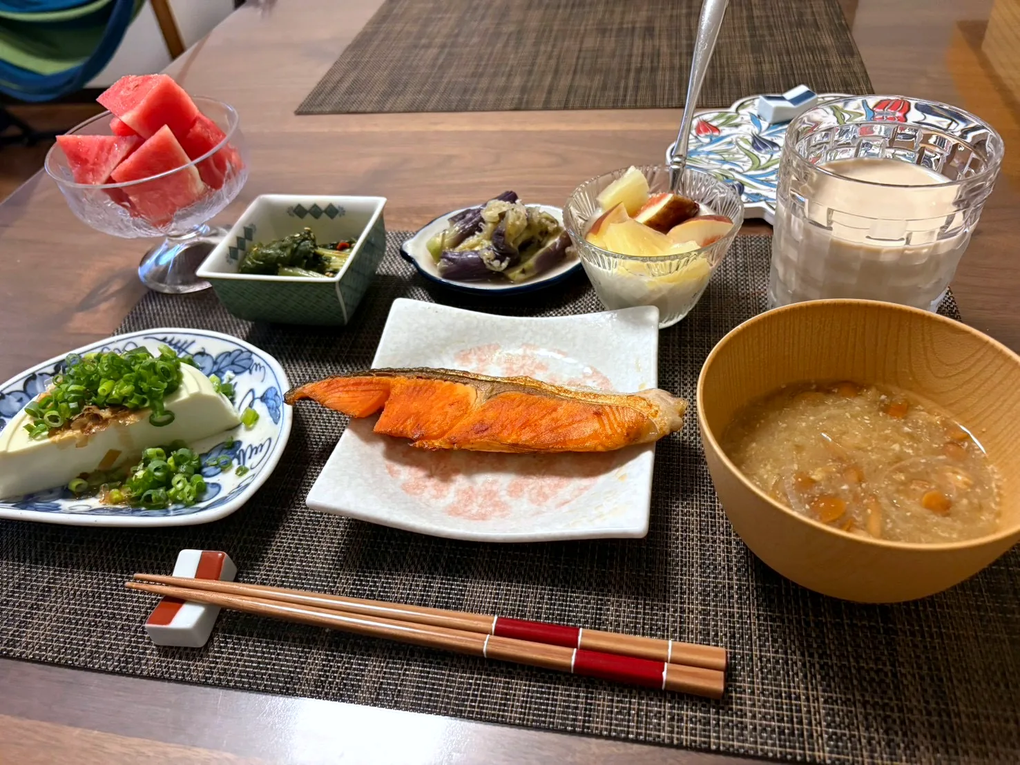 Japanese breakfast with grilled salmon, cold tofu topped with green onion, soup in a wooden bowl, small side dishes and watermelon