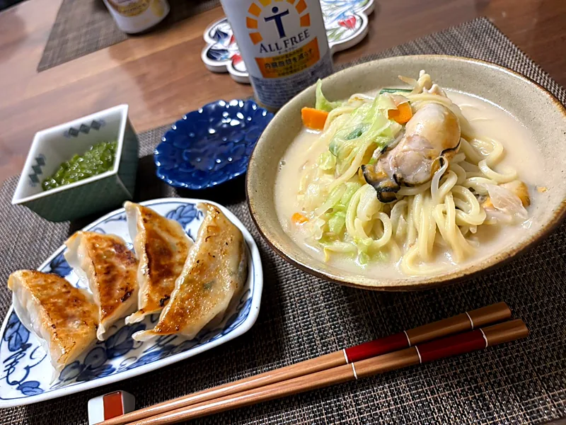 Pan-fried gyoza on a blue and white plate beside a bowl of noodle soup with oysters, cabbage and carrot