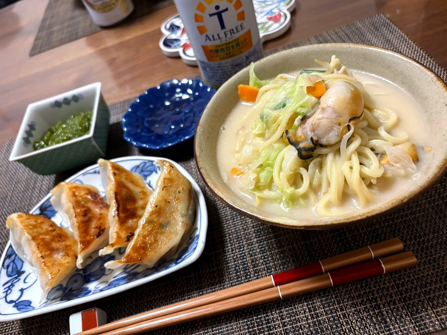Pan-fried gyoza on a blue and white plate beside a bowl of noodle soup with oysters, cabbage and carrot