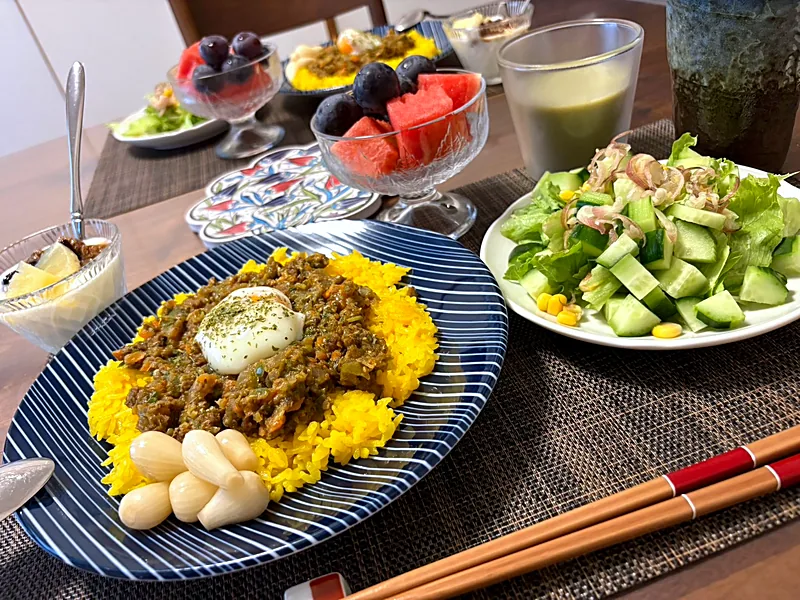 Keema curry on yellow rice topped with a soft egg, with a green salad and a glass bowl of watermelon and grapes