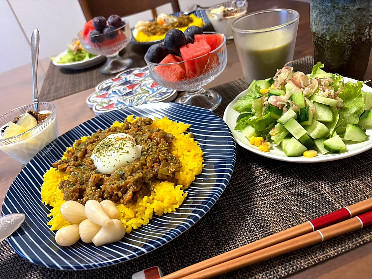 Keema curry on yellow rice topped with a soft egg, with a green salad and a glass bowl of watermelon and grapes