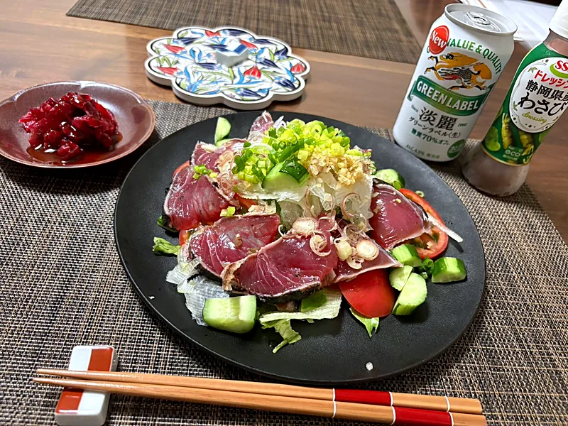 Slices of seared bonito over lettuce, cucumber and tomato, topped with sliced onion, green onion and grated ginger, with a can of beer