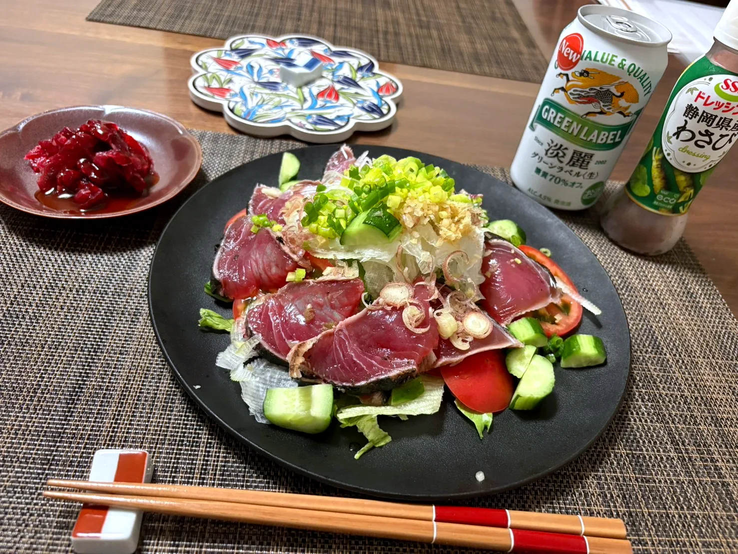 Slices of seared bonito over lettuce, cucumber and tomato, topped with sliced onion, green onion and grated ginger, with a can of beer